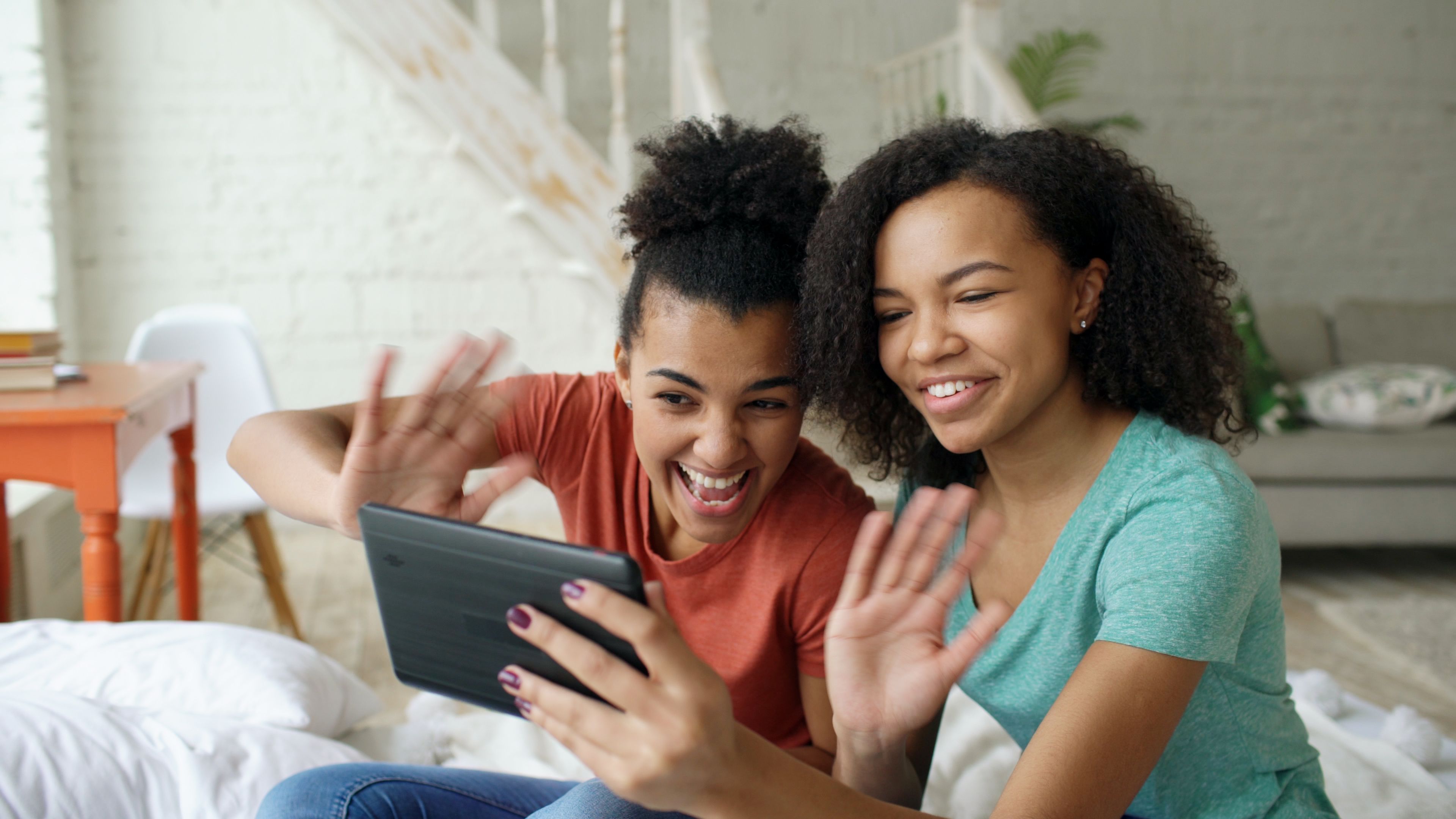 Two people smiling and waving during a video call on a tablet